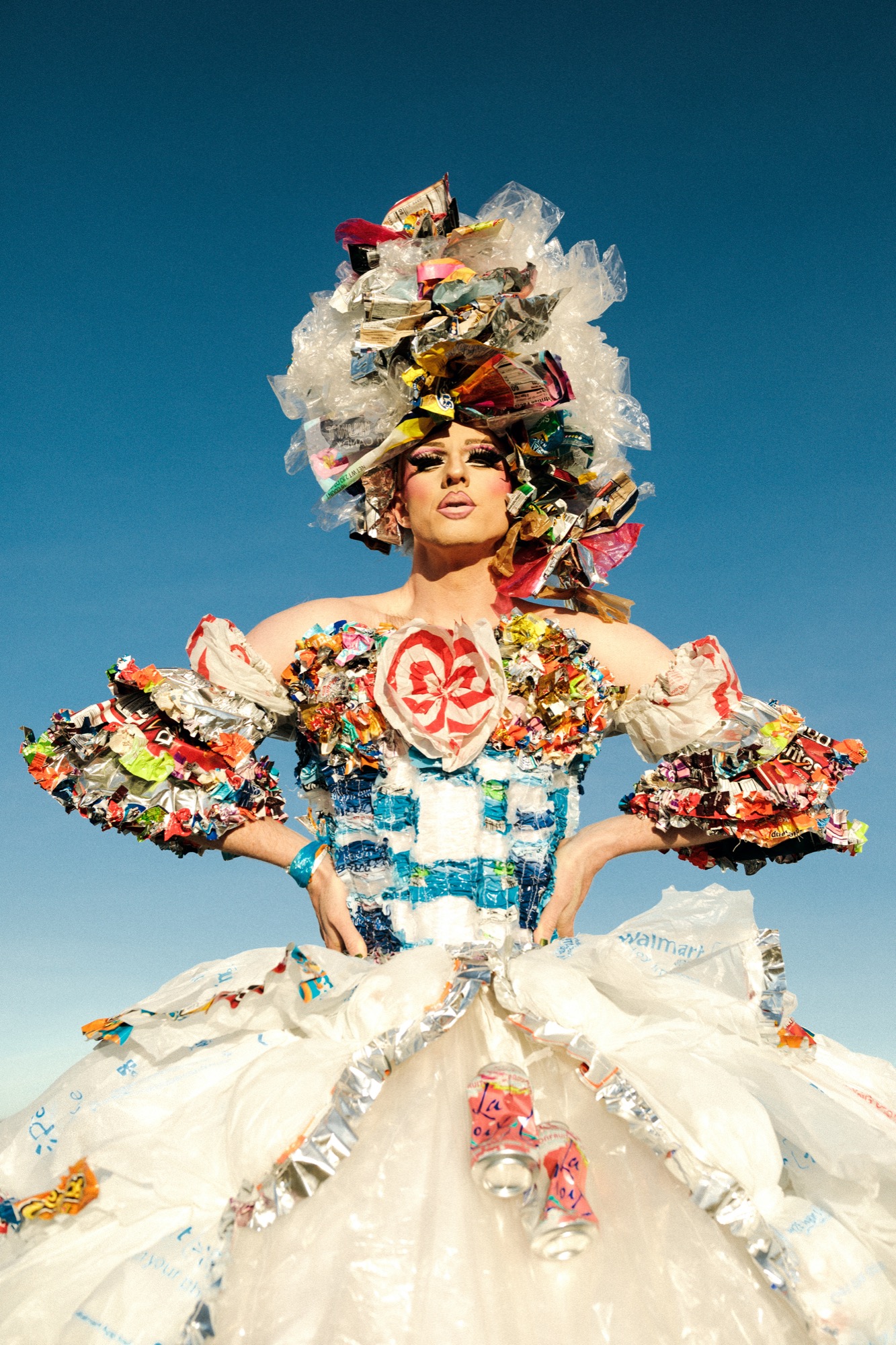 a white drag queen posing outside wearing a dress made up of pieces of trash