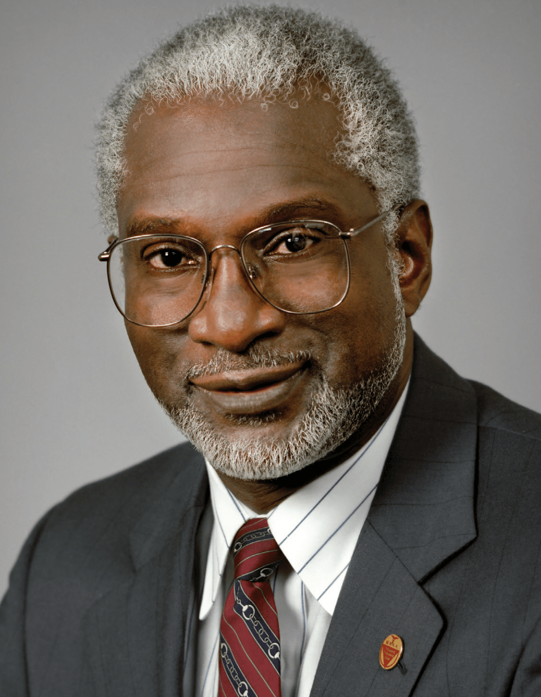 an older black man in a suit and a tie wearing glasses posing for a portrait photo