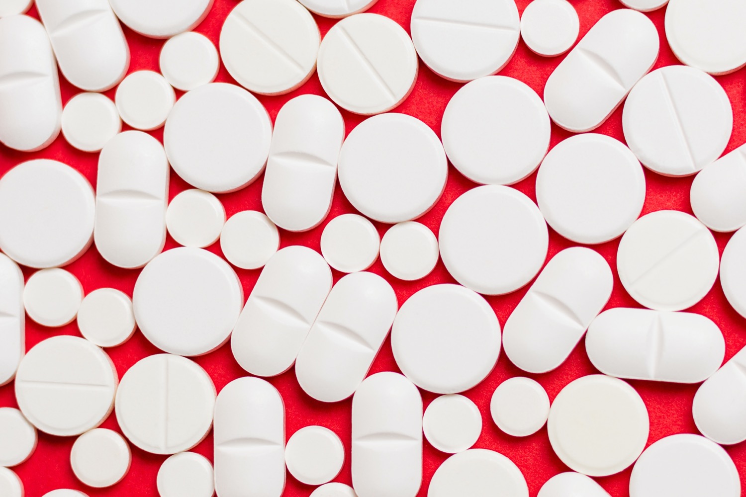 dozens of white pills of different shapes and sizes on a red background