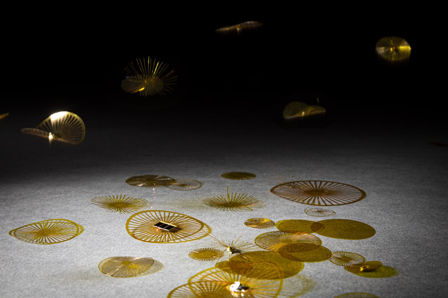 a table with circular yellow transparent preforated strips of plastic with tiny electronics in their center. some float in the area above the table