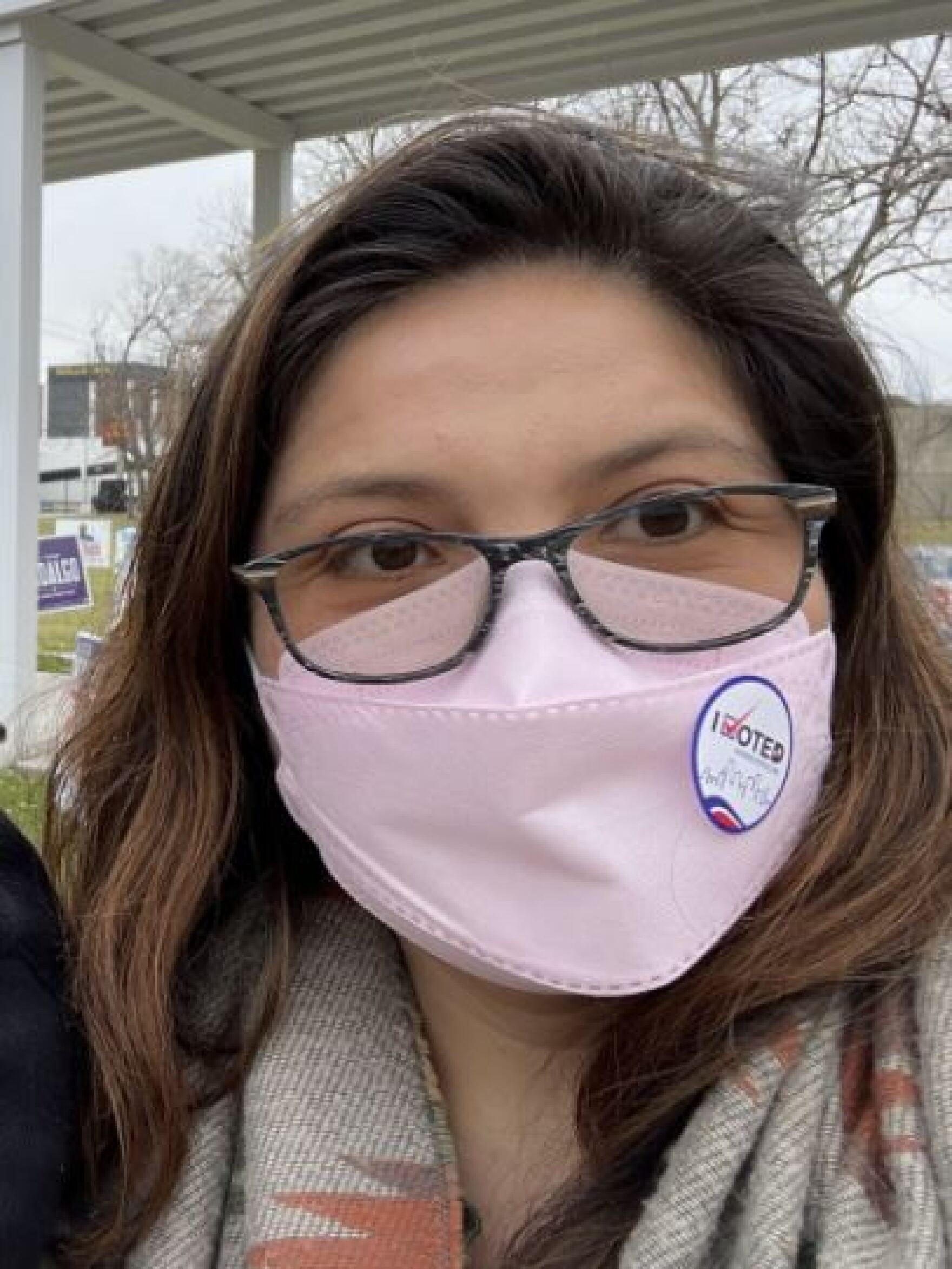a selfie of a latina woman wearing glasses and a pink face mask outside