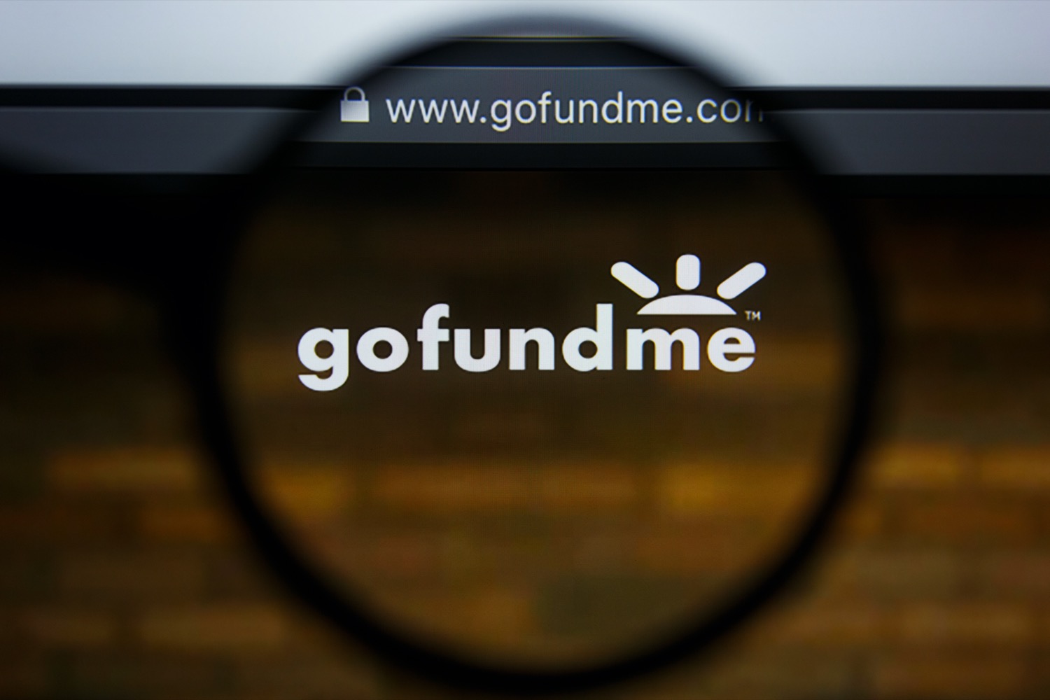 a picture of a computer screen of the gofundme home page with a magnifying glass over the text 'gofundme'