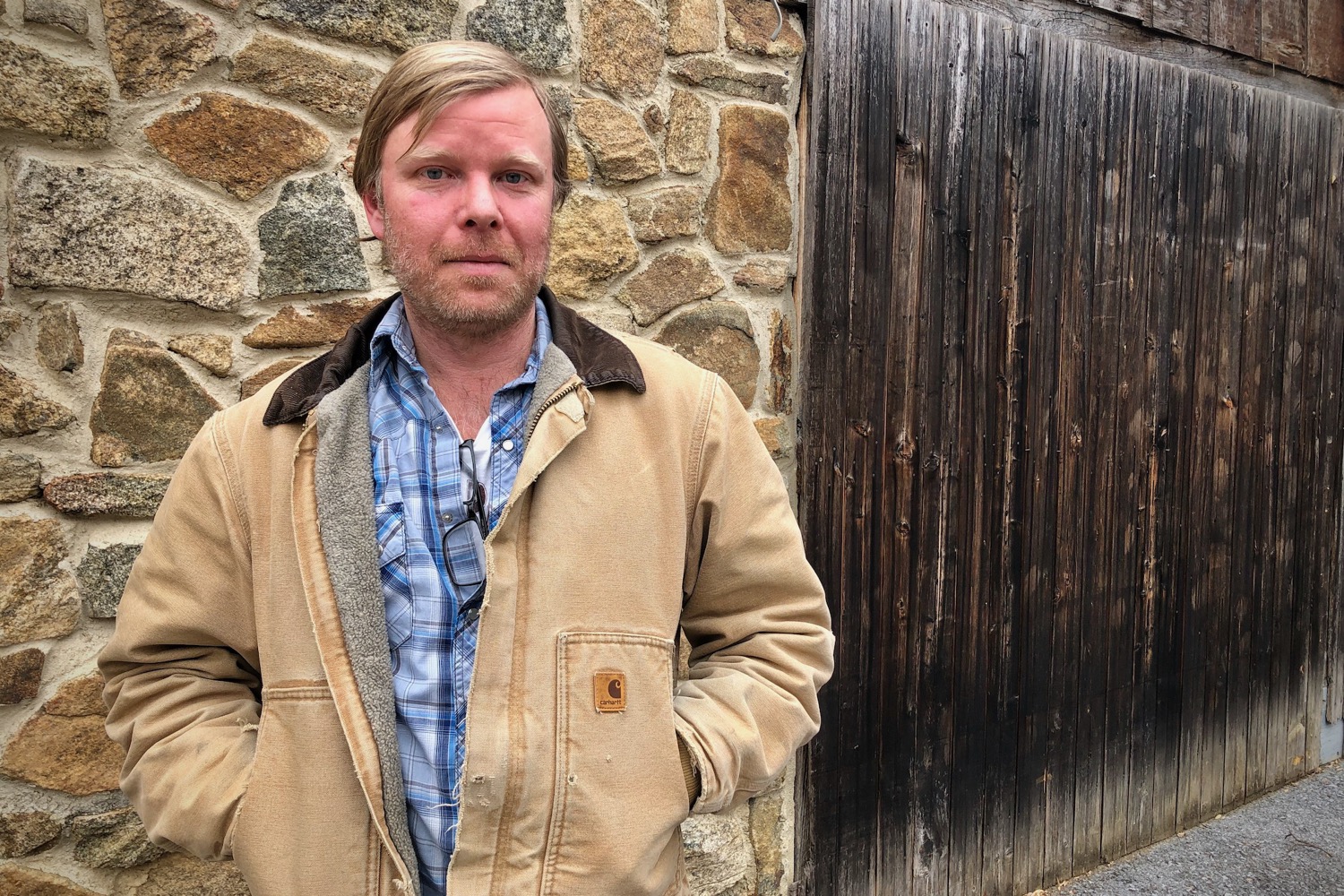 a white man with short blonde hair wearing a jacket looks at the camera pensively