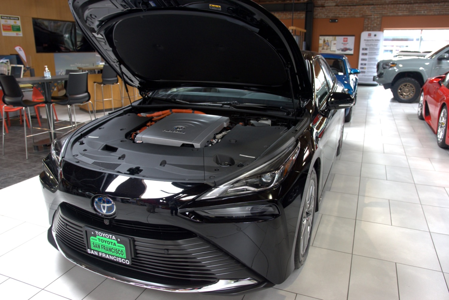 a normal looking black toyota sedan in a car showroom. the hood is up, revealing a very simple layout, with a large rectangular metal housing for the hydrogen engine