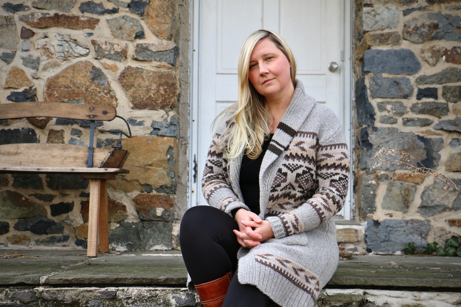 a white blonde-haired woman sitting on stone steps of a stone house, looking pensive at the camera