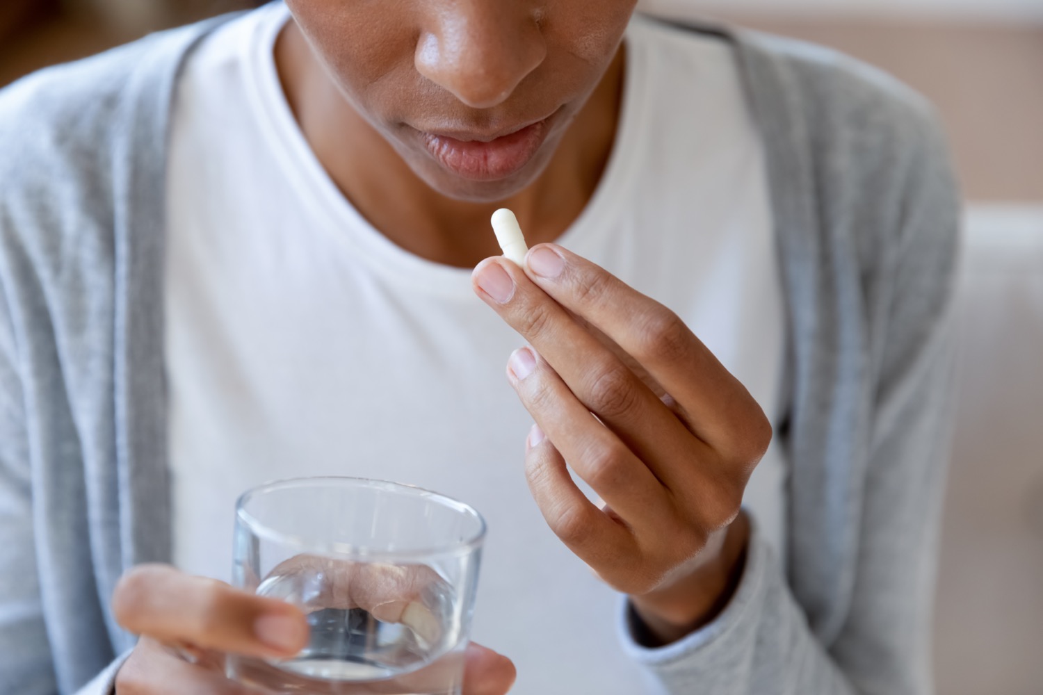 a black woman about to take a pill, holding a glass of water in the other hand