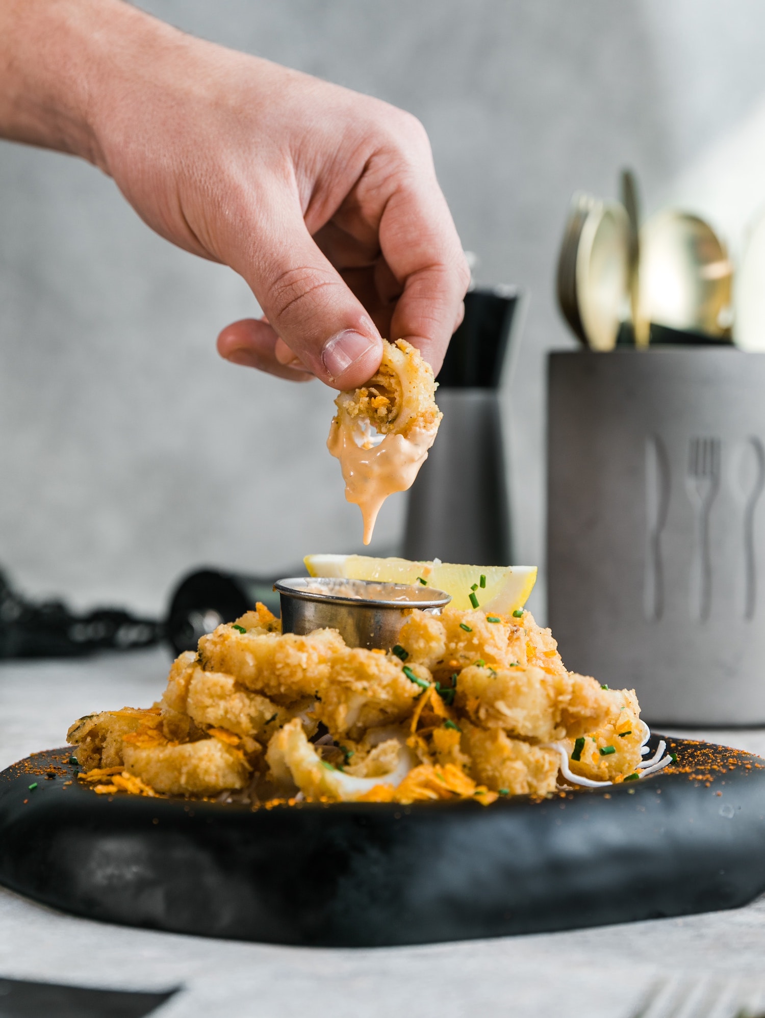 a person picking up a piece of calamari in sauce from a plate