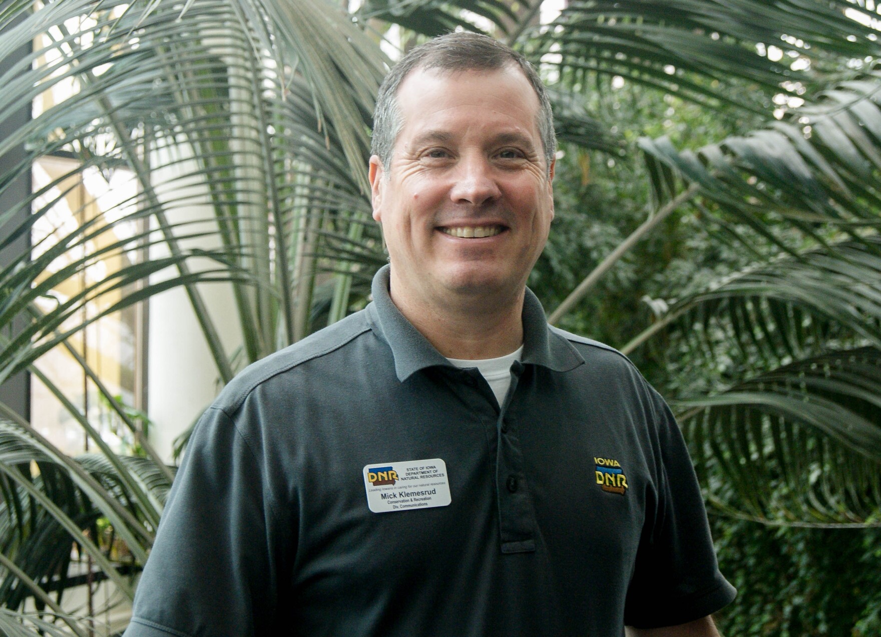 A man smiling at the camera in front of some leafy indoor plants.