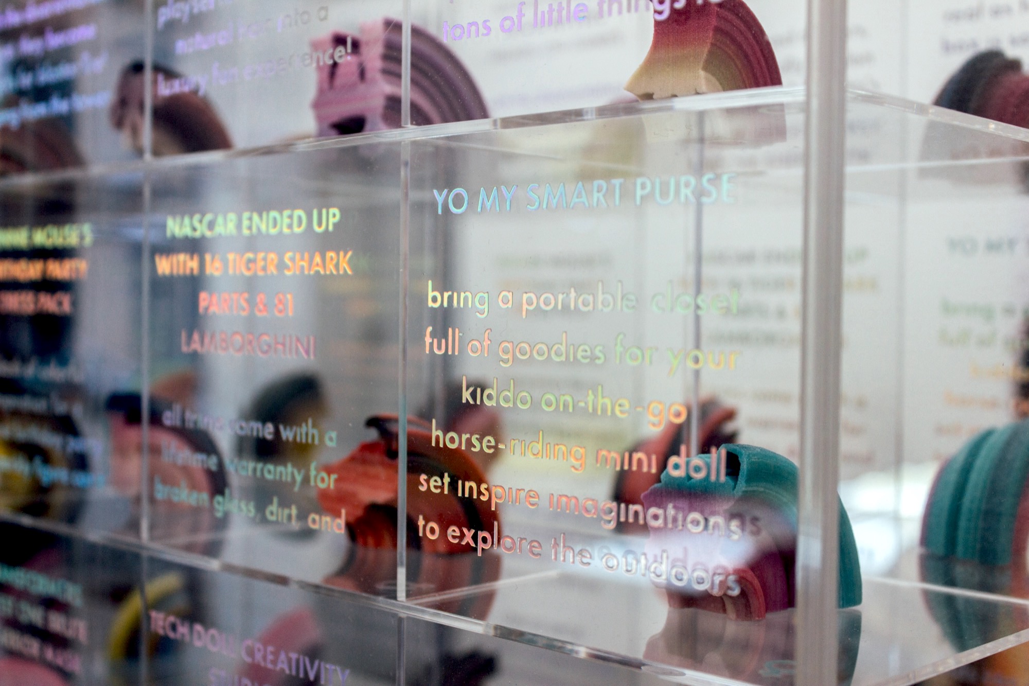 rows of clear plastic tiny square containers each filled with a one inch tall abstract 3d print of a toy. rainbow holographic text is on each square, the one closest to the camera says 'yo my smart purse'