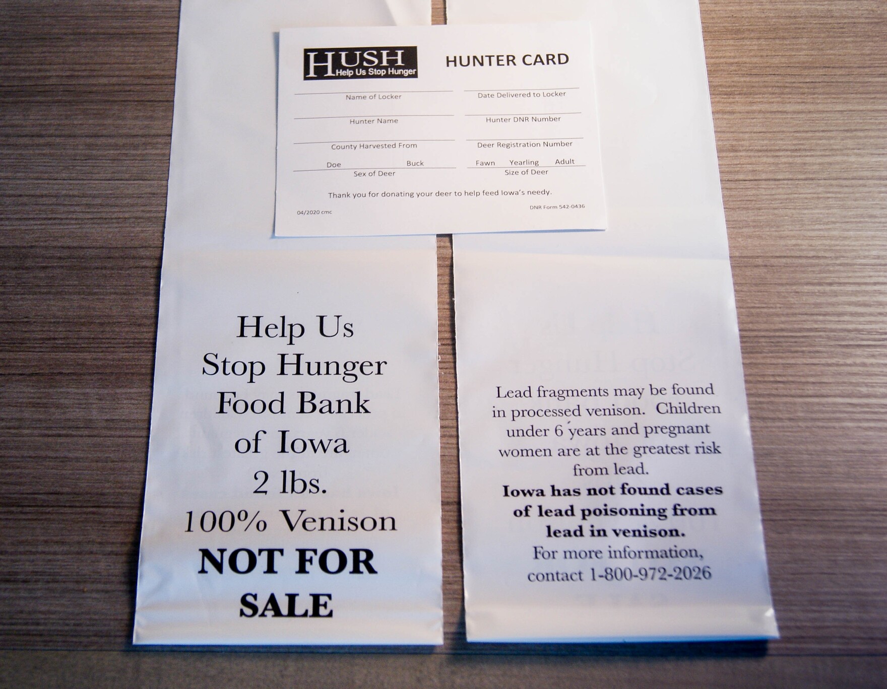 Two sheets of paper that read: "Help us stop hunger. Food Bank of Iowa, 2 lbs. 100% Venison NOT FOR SALE. Lying on top, a small piece of cardstock labeled "Hunter Card"
