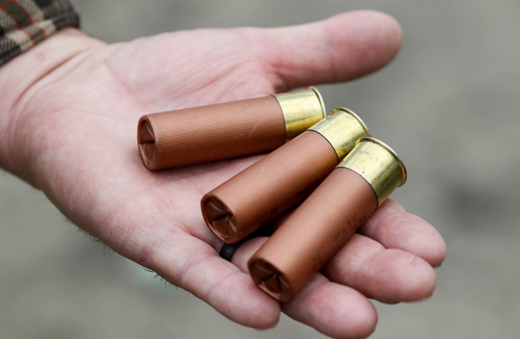 A hand holding three large copper bullets