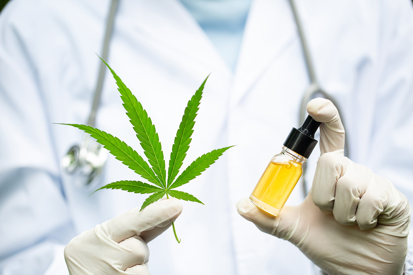 A doctor in a lab coat holding up a marijuana leaf and CBD oil.