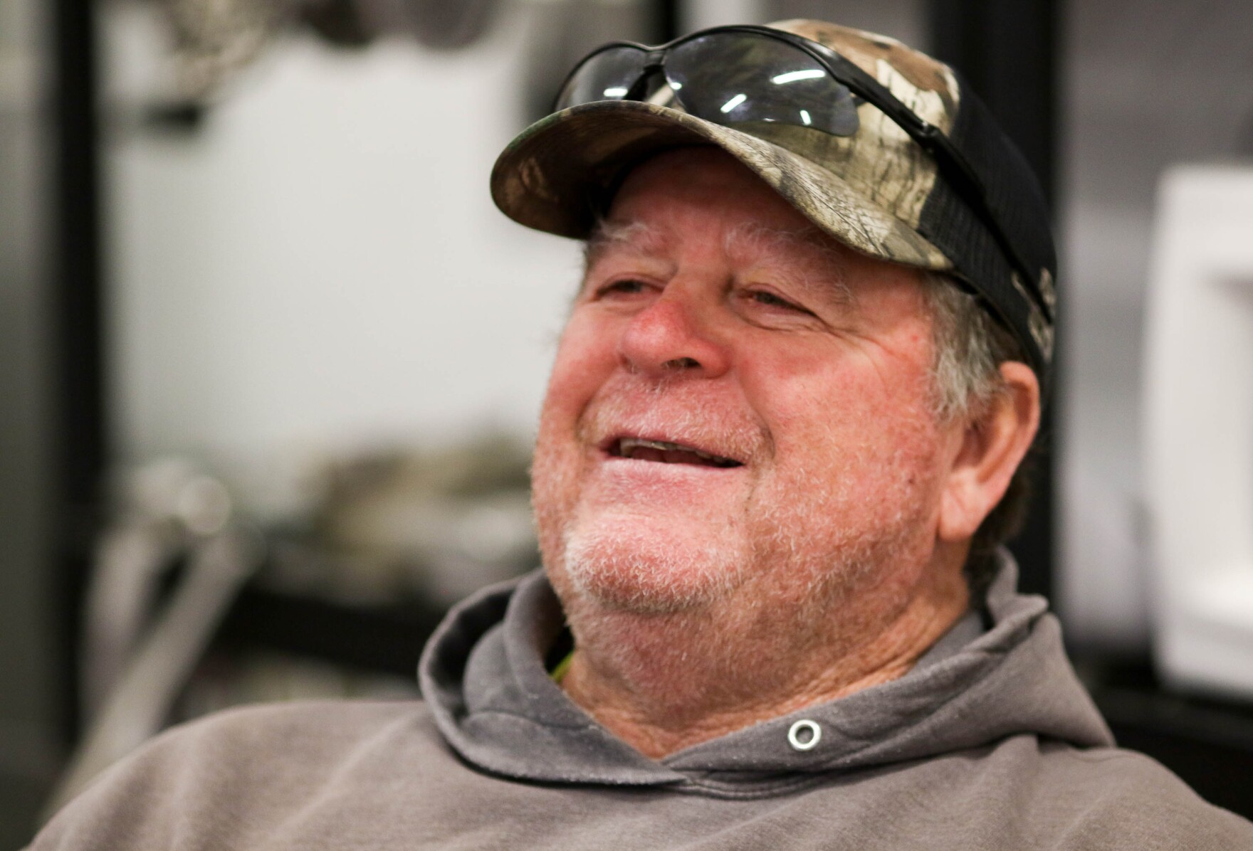 A man with a camo-print hat smiling and looking to the left of the camera.