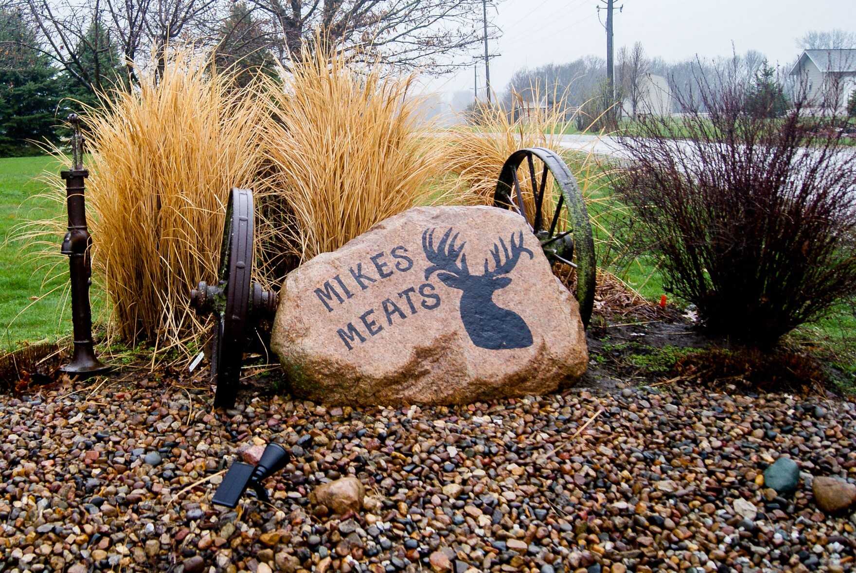 A garden area where a large rock is painted to say 'Mikes Meats" with a picture of a buck.