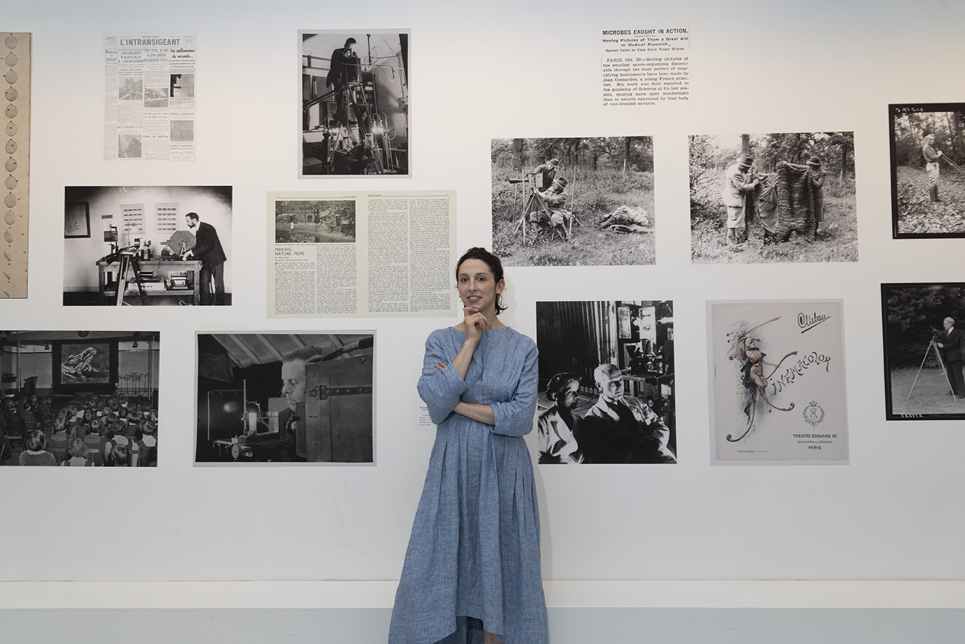 A woman stands in front of a wall of black-and-white images and text showing the history of early science films. 