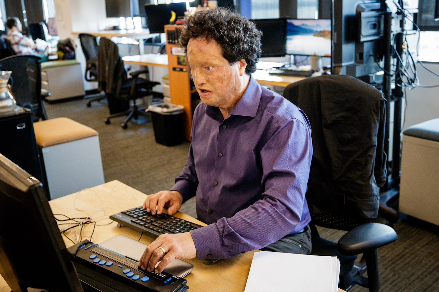 At an Amazon office, Josh Miele works on the computer at his desk and uses a refreshable braille display.