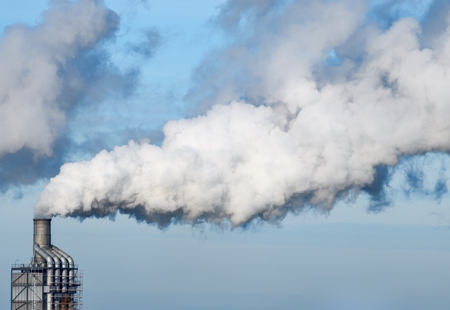 a factory with billowing smoke or gas coming out of a stack, filling up most of the image