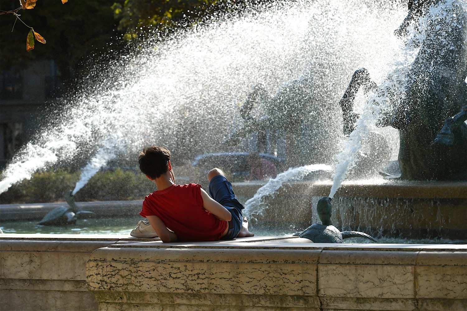a young white man reading by a fountain during the hot weather in Paris France.