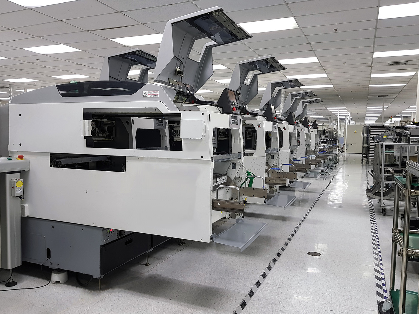 A line of large, off-white machines used to manufacture electronics in a brightly-lit factory with a low ceiling.