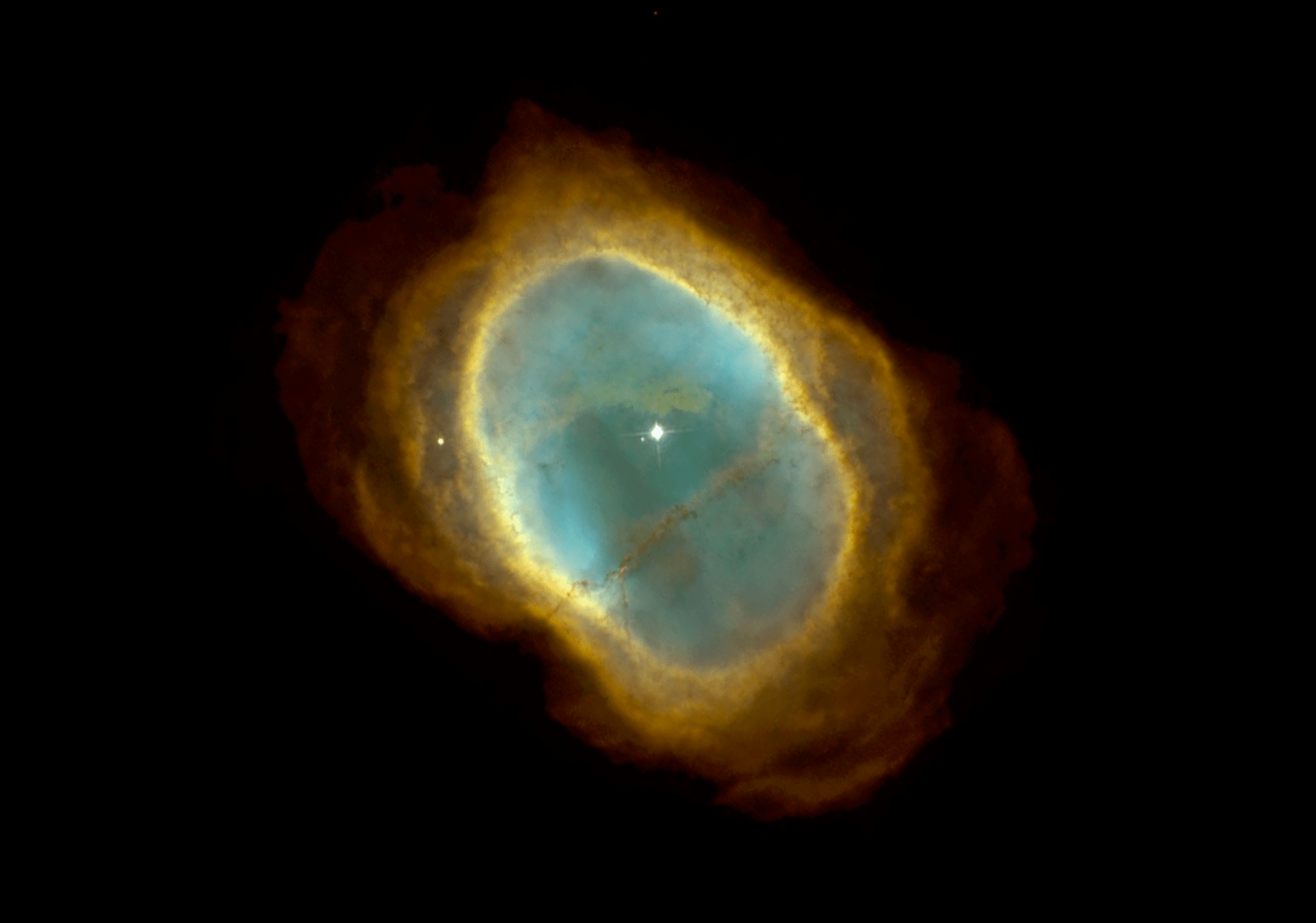 This Hubble image clearly shows two stars near the center of the nebula, a bright white one and an adjacent, fainter companion to its upper right. A third, unrelated star lies near the edge of the nebula. The flood of ultraviolet radiation from the faint star’s surface makes the surrounding gases, radiating out from the stars in an oval, glow through fluorescence. The colors were chosen to represent the temperature of the gases. Blue represents the hottest gas, which is confined to the inner region of the nebula. Red represents the coolest gas, at the outer edge. Also revealed is a host of filaments, including one long one that resembles a waistband, made out of dust particles which have condensed out of the expanding gases.