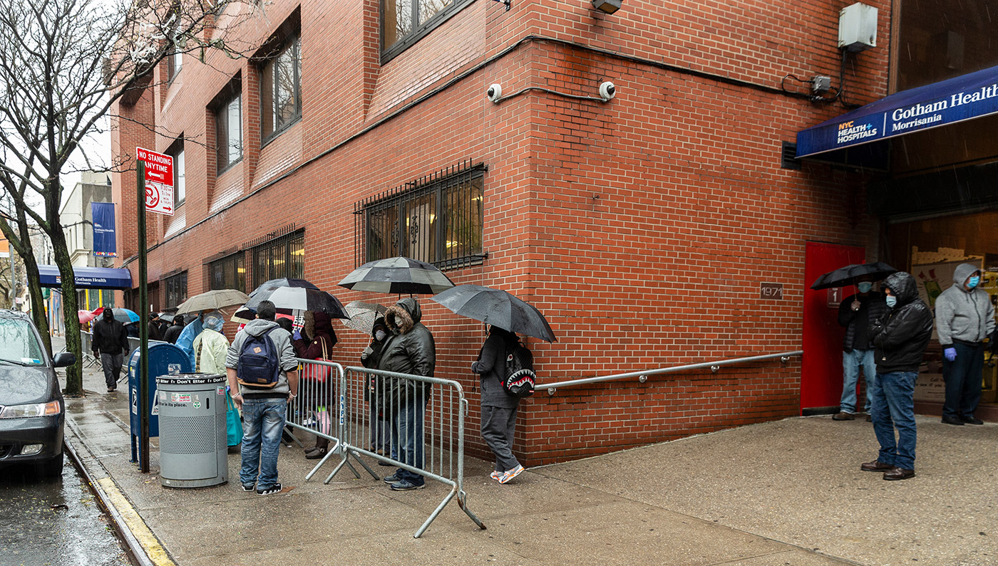 a group of people with umbrellas waiting in line in front of a hospital