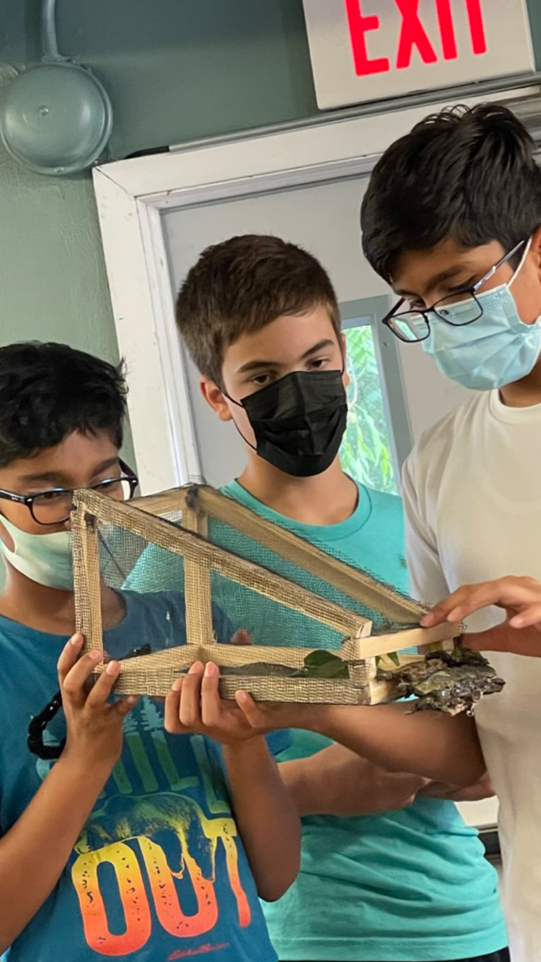 Photo of three middle school students standing with handmade wooden traps in their hands