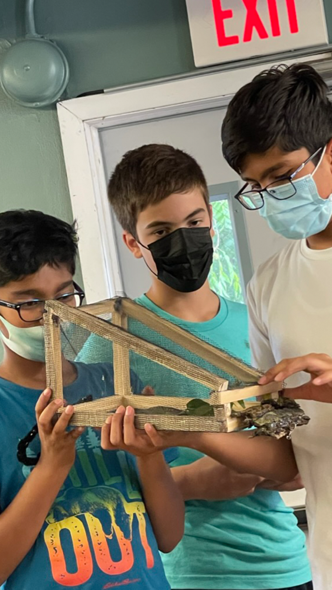 photograph of three middle school-aged students, standing and holding in their hands a handmade, wooden trap