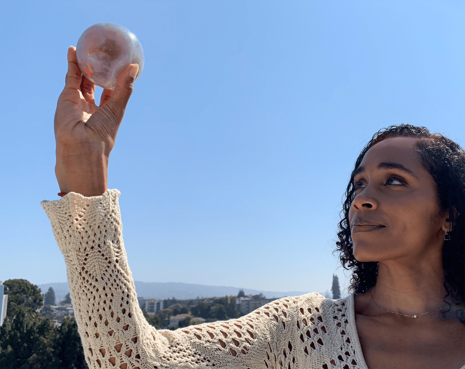 a black woman wearing a white long sleeve top holds up a 3d printed sphere the size of an apple that has the pattern of a marble