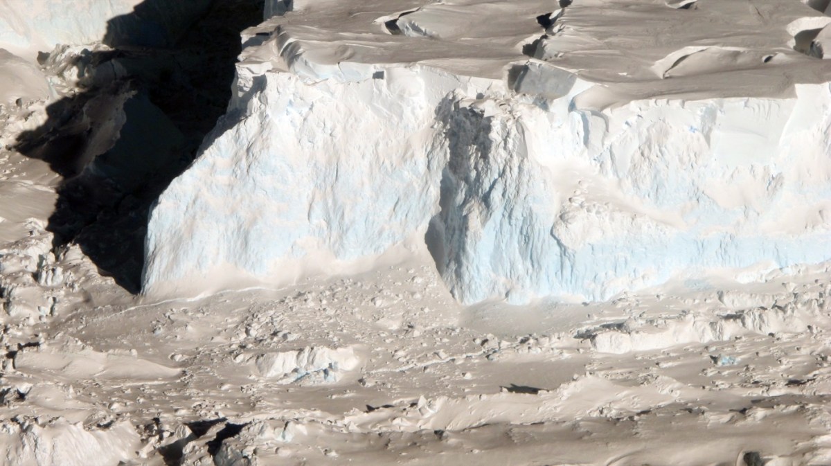 A large rough pair of ice cliffs of the Thwaites Glacier rest on a wash of ice and snow in late afternoon light in a photo taken from an aircraft flying overhead in 2012