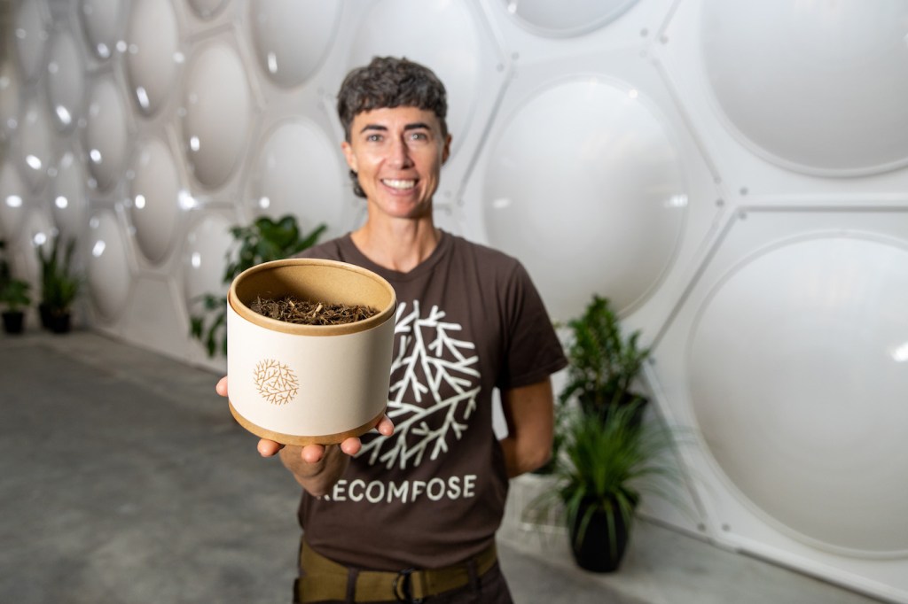 A woman holds a white pot of soil out towards the camera.