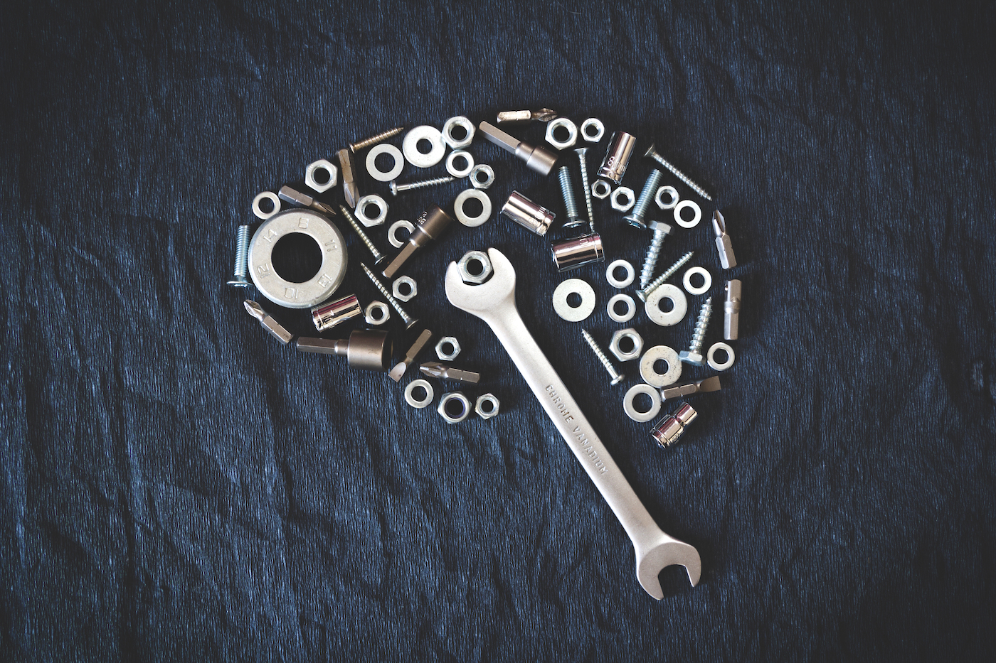 washers and nails shaped into the silhouette of a brain. A wrench reaches inside and twists one of the washers