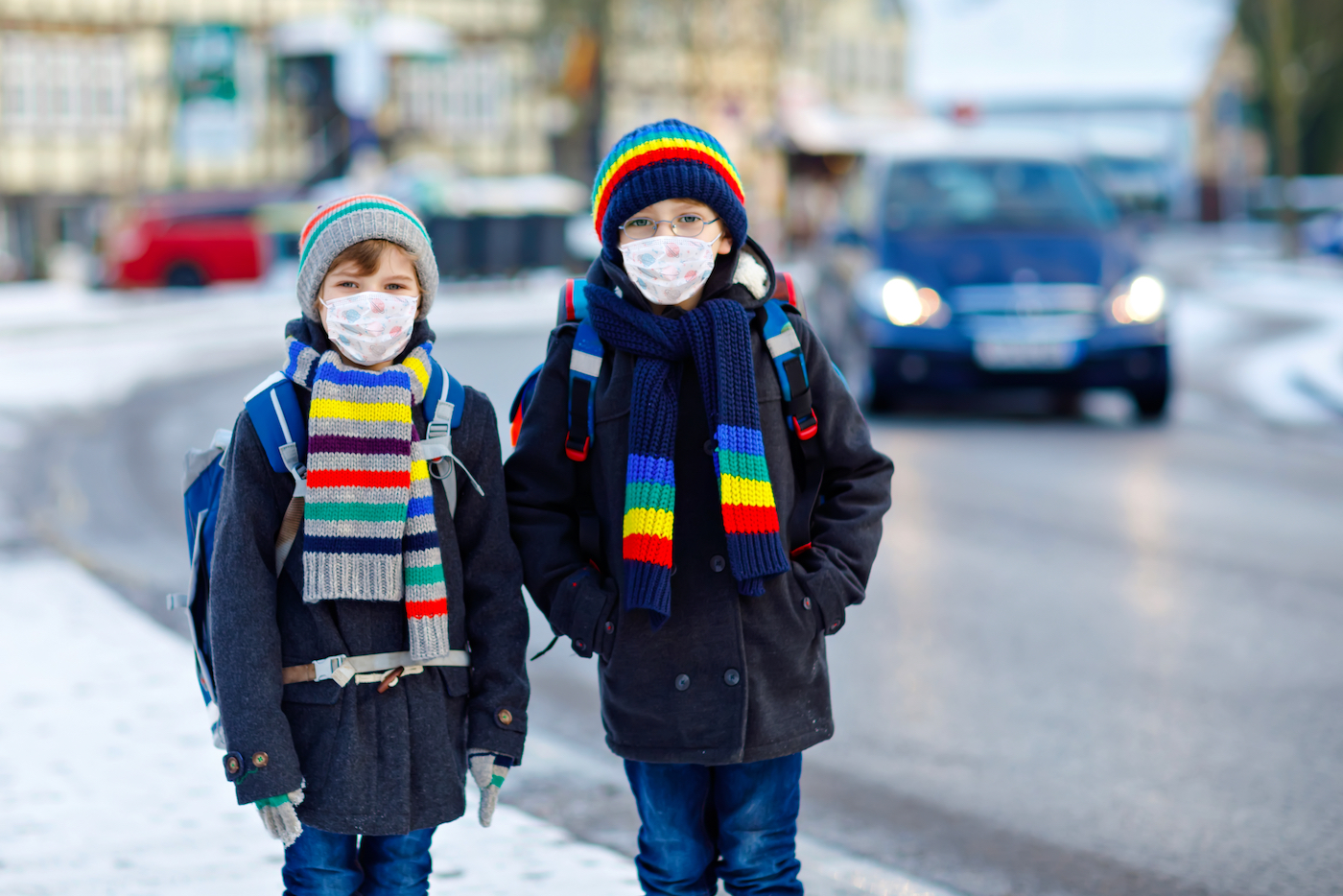 Two kids boys wearing medical mask on the way to school. Children with backpack satchel. Schoolkids on cold winter day with warm clothes. Lockdown and quarantine time during corona pandemic disease