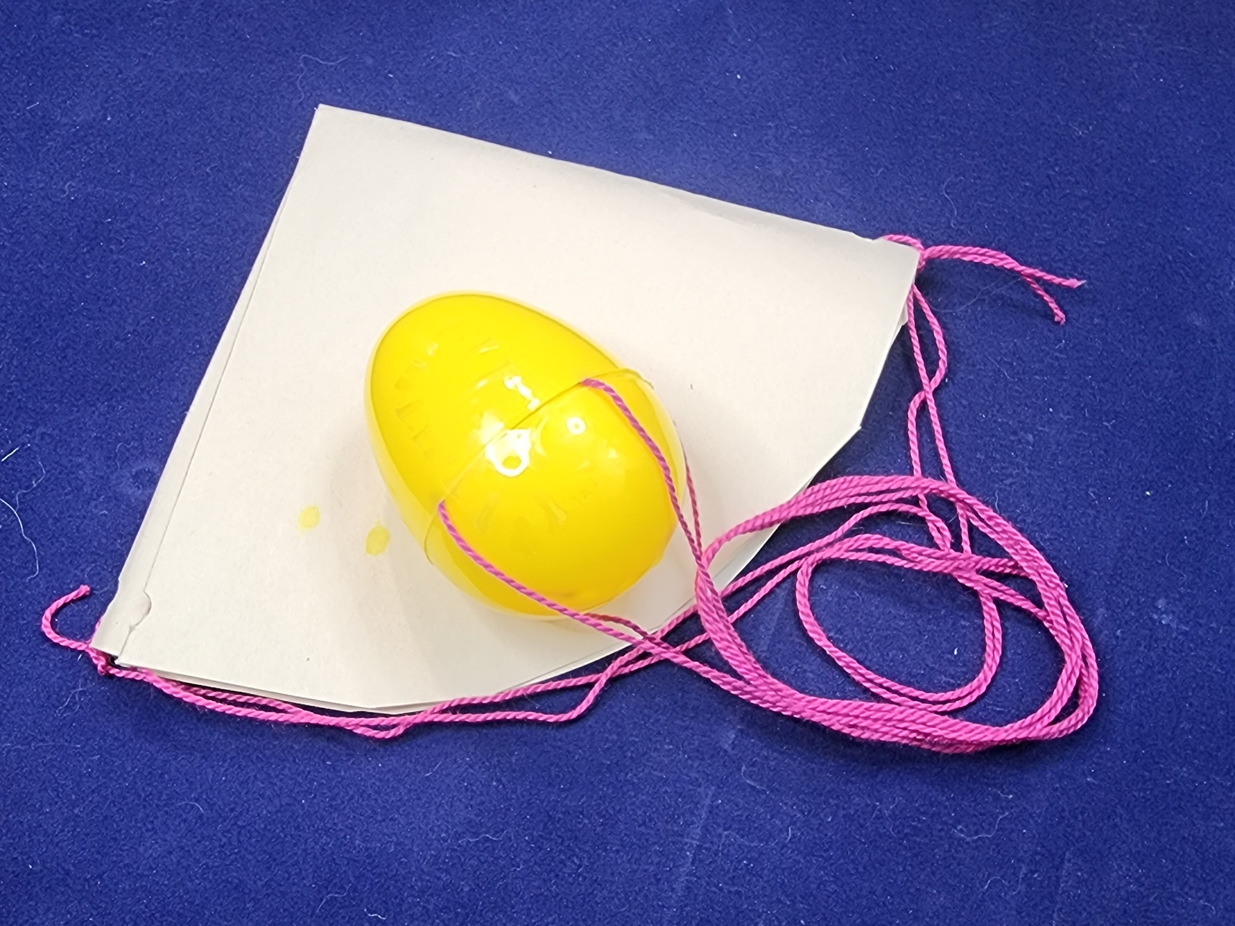 A plastic egg with strings attached which connect to a paper parachute.