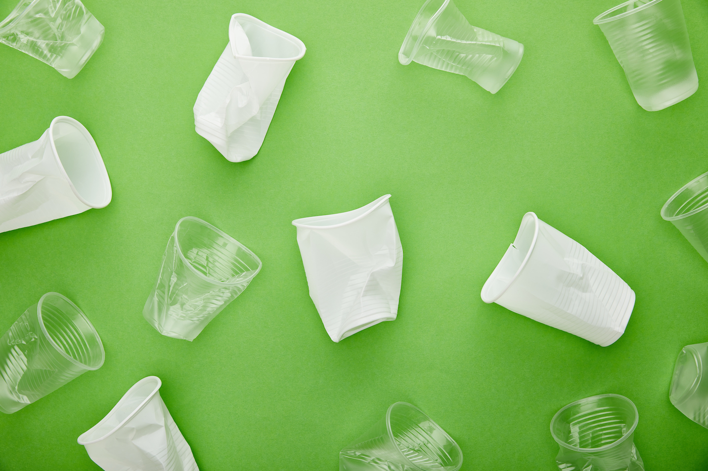 top view of disposable white and transparent plastic cups on green background