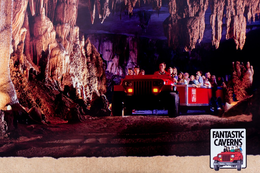 Children and families riding in a red tram through a wide cavern mouth. 