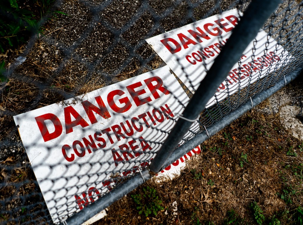 Two signs behind a wire fence that read "Danger Construction Area"