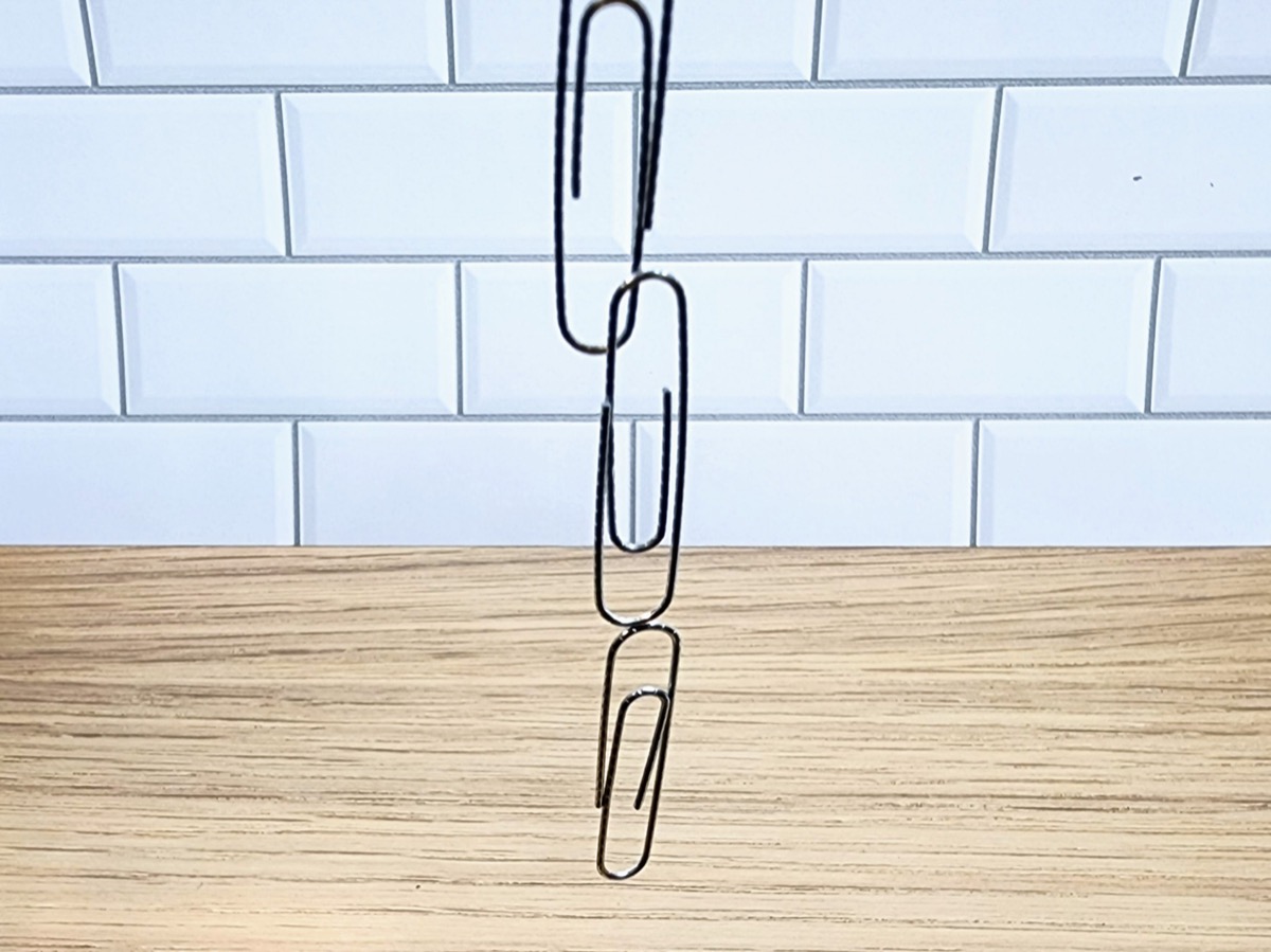 Three paper clips hanging from a magnet.