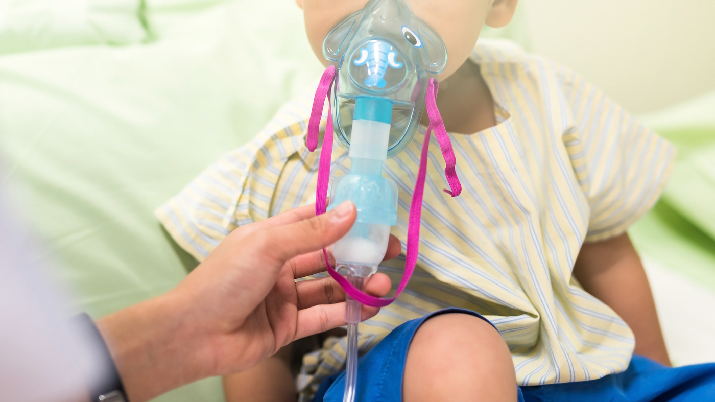 The lower third of a child's face is visible. Sick young boy, 3 years old, inhaling medication by inhalation mask to cure Respiratory Syncytial Virus (RSV) on hospital bed.