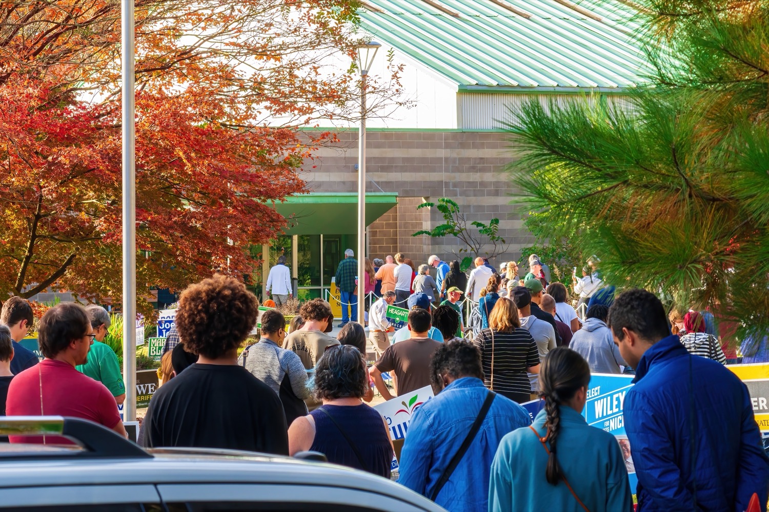 a long line of dozens of people lining up in front of a building with trees bordering it