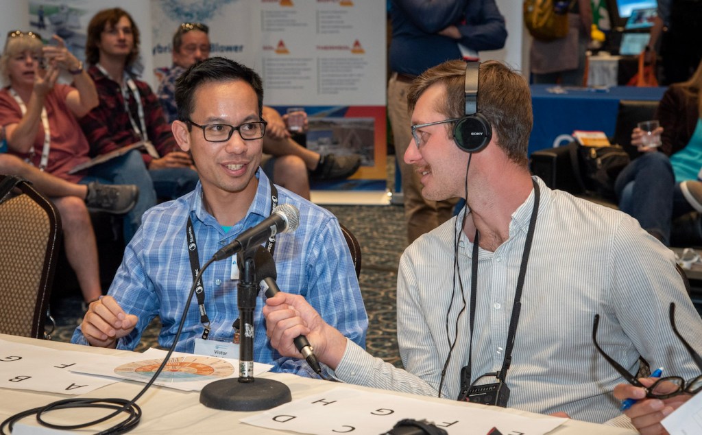 Two men by a mic talk to each other. 