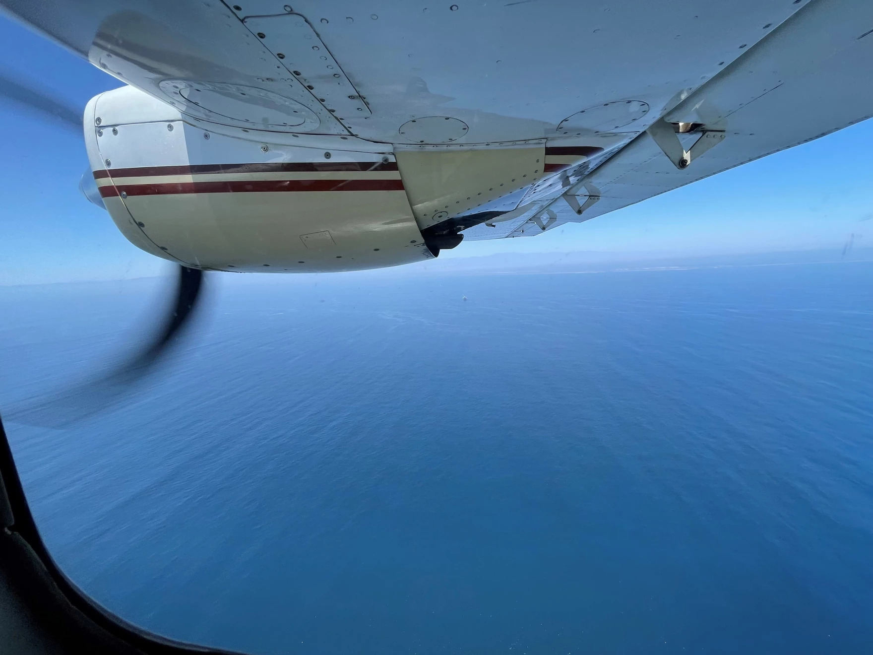 looking out the window of a small propellor plane. the window is directly beneath the wing. the view is just ocean