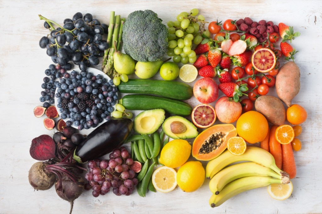Assortment of rainbow fruits and vegetables, berries, bananas, oranges, grapes, broccoli, beetroot background on white table arranged by color. 