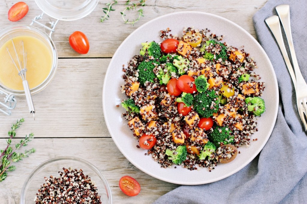 A bowl of quinoa salad with tomatoes and broccoli and a side of dressing. 