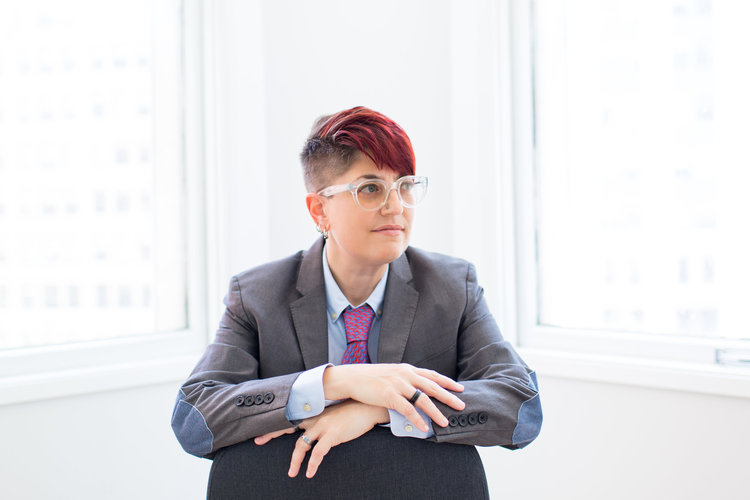 A person in a business suit sits in a clean white office, looking out to the right.