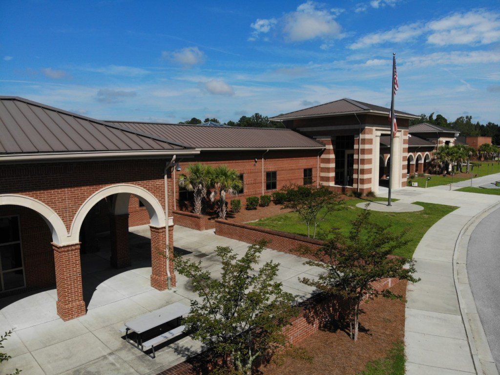 A sunny day at Richmond HIll Middle School, a brick building with stone archways surrounded by palms and green grass.