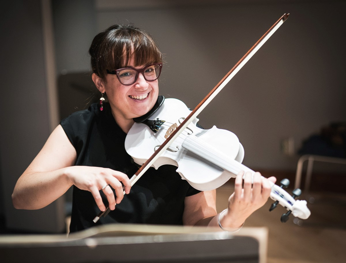 A woman smiling at the camera as she plays a bright white violin.