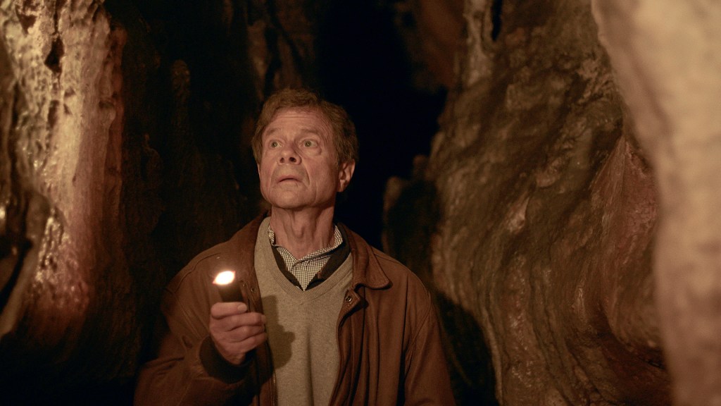 A man shining a flashlight to see the walls of a cave. 