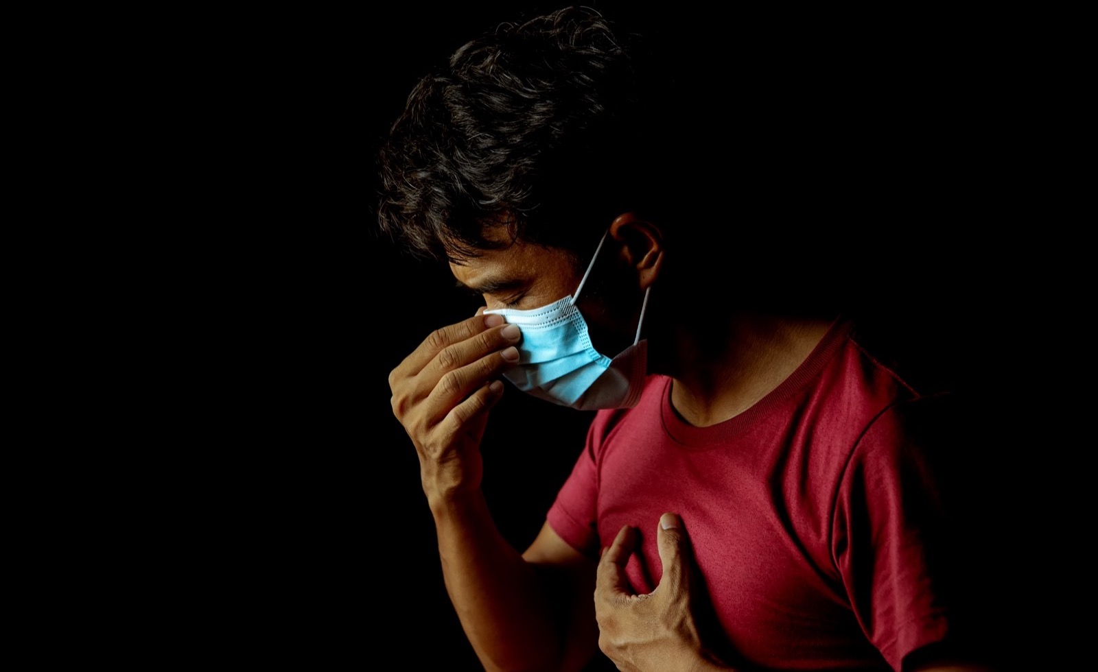 a man against a black background touching his face mask and putting a hand to his chest