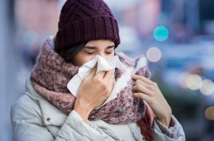 Young woman blowing her nose with a tissue outdoor in winter. Young woman getting sick with flu in a winter day. 