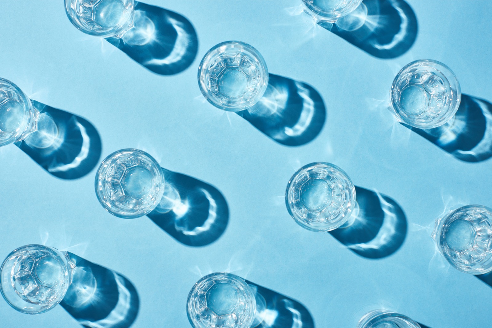 a top down view of 11 water glasses against a blue background/table